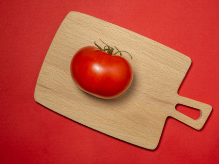 Tomato on colored paper. Greenhouse tomato on a kitchen small board. Bright vegetable background.