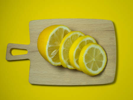 A sliced lemon  on a small cutting board on a yellow background. Citrus on the table. Bright background. Healthy fortified food for a diet. sour product.の写真素材