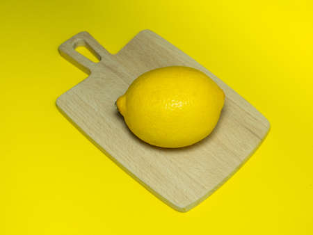 A whole lemon on a small cutting board on a yellow background. Citrus on the table. Bright background. Healthy fortified food for a vegetarian.の写真素材