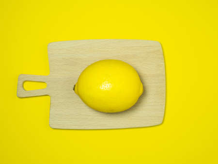 A whole lemon on a small cutting board on a yellow background. Citrus on the table. bright background. Healthy fortified food for a vegetarian.の写真素材