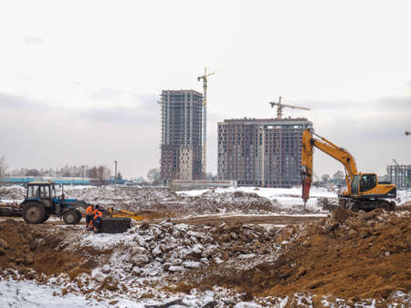 Construction of high-rise buildings in winter. The work of excavators. land works. Digging pits. Concrete building frames. mountains of the earthの写真素材