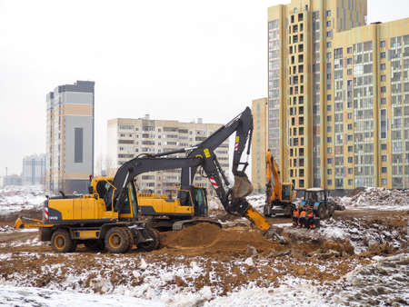 Construction of high-rise buildings in winter. The work of excavators. land works. Digging pits. Concrete building frames. mountains of the earthの写真素材