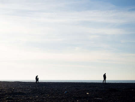 People on the spring pebble beach at sunset. Silhouettes of people on the shore. vacation on the beach. Rest on the sea. rocky shore. Pebble beach.の写真素材