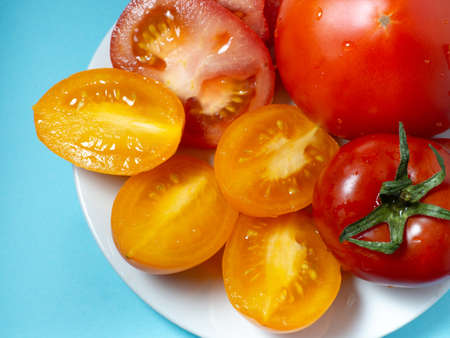 Sliced ââjuicy tomatoes of different varieties on a plate. Greenhouse orange tomatoes on a blue background. Health food. Vegetarian food. Still life vegetablesの写真素材