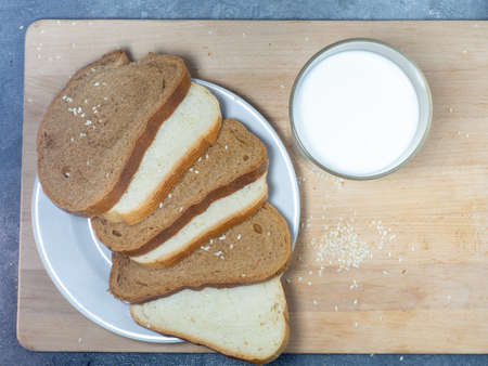 Pieces of rye and white bread with a glass of milk on a plate. Healthy breakfast. Bakery products with sesame seeds.の写真素材