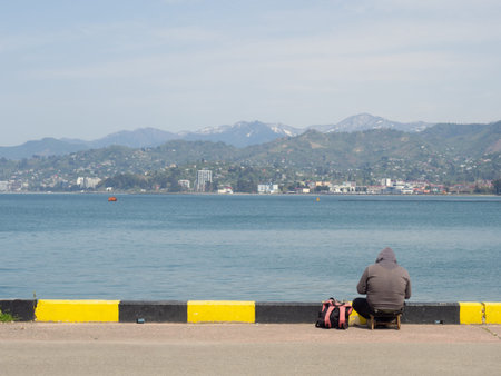 Fisherman on the pier on the seashore. melancholy setting. A man is sitting on the beach with a...