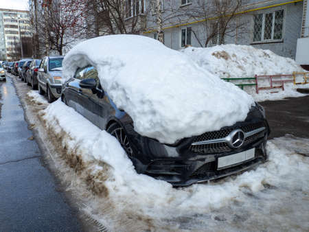 street photo. Big snowdrifts in the city. Thick layer of snow on the car. after bad weatherの写真素材