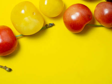 Sweet cherry with a stem on a yellow background. bright table. Natural berries on the table. harvest. Cherries of different varieties. Place for an inscriptionの写真素材
