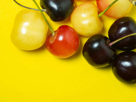 Sweet cherry with a stem on a yellow background. bright table. Natural berries on the table. harvest. Cherries of different varieties. Place for an inscriptionの写真素材