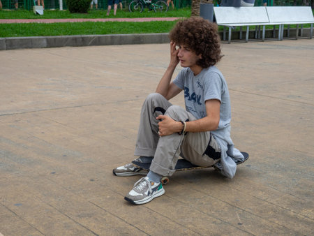 Batumi, Georgia. 07.19.2022 Curly guy sits on a skateboard. sports. Skateboarding. relaxation. Youth environment. Teenagerのeditorial素材