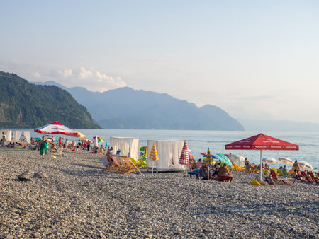 Gonio, Georgia. 03/08/2022 Pebble public beach on the Black Sea coast. Lots of people on the water. People on deck chairs and under umbrellas. Hot evening in Batumi. beach resort. Relaxation under the sunのeditorial素材