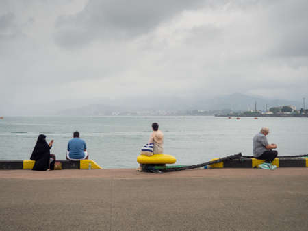 Batumi, Georgia. 08. 18.2022 People are sitting on the pier. Quiet rest. People sit separately. At the seaport. Rest in cloudy weather at sea.の写真素材