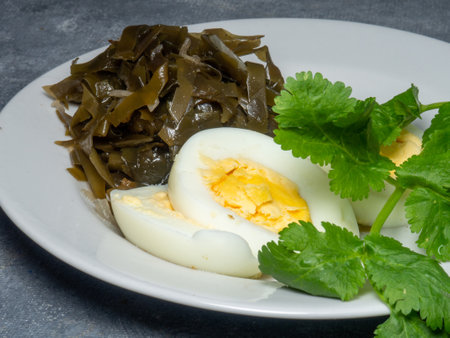 Seaweed salad and cut boiled egg. Dish on the table in a plate. Pepper half of an egg. Parsley greens as decoration. Healthy snack foodsの写真素材