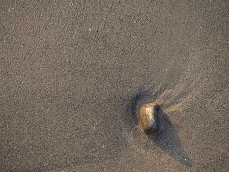 One stone on a background of black sand. The silence of the wild beach. Stones on the sandy beach. Black sand in the sun. Quiet place. The silence of the waves Edge of the coast. Black sand on the beach. bathing place.の写真素材