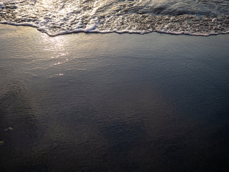 Wet sand of the beach in the rays of the setting sun. The silence of the wild beach. Natural background. Black sand in the sun close-up. Quiet place. Edge of the coast. Bathing place. Waveの写真素材