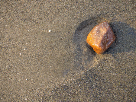 One stone on a background of black sand. The silence of the wild beach. Stones on the sandy beach. Black sand in the sun. Quiet place. The silence of the waves Edge of the coast. Black sand on the beach. bathing place.の写真素材