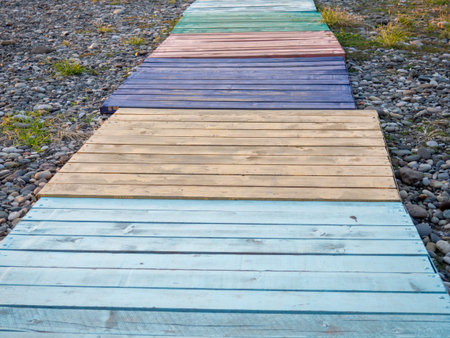 Multi-colored decking on a pebble beach. The path to the shore from different colored boards....