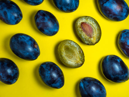 Plums on a yellow background. Juicy sliced ââplum. Stone in yellow pulp. Healthy food concept. Sweet purple variety. fruit pattern. A handful of fruit.の写真素材