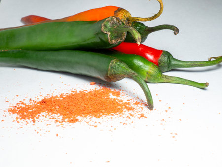 The green pepper and ground red pepper are isolated. Sharp pepper on a white background. Ingredient for a burning dish. Paprika scattered on the tableの写真素材