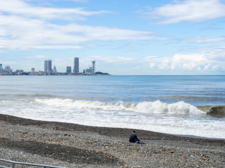 Lonely man in bad weather on the seashore. sadness and sadness. The concept of loneliness. Man on the beach against the backdrop of the cityの写真素材