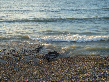 Coastline. Waves gently roll on the shore. Pebble and black sand beach. big boulder. Top view of the wavesの写真素材