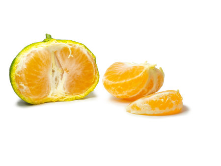 Unripe tangerine. Peeling a tangerine. Green fruit on a white background. Sour ingredient. Citrus isolate. Sliced green mandarin. Useful fruit.の写真素材