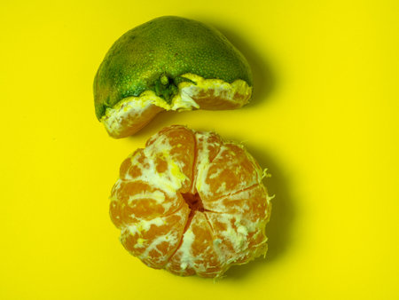 Unripe tangerine on a yellow background. Peeling a tangerine. Green and yellow color. Sour ingredient. Citrus isolate. sliced tangerine. Useful fruit. citrus concept.の写真素材