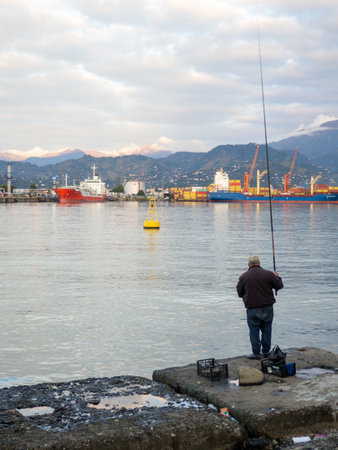 Fisherman on a concrete pier. A fisherman in the port catches fish. city fishing. hobby men. Atmosphere of an Asian port.の写真素材