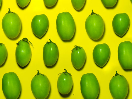 Green tomatoes on a yellow background. The concept of an unripe vegetable. background from green vegetables. Salting product. healthy foodの写真素材