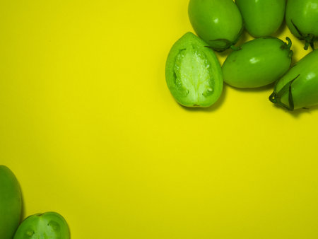 Green tomatoes on a yellow background. The concept of an unripe vegetable. Background from green vegetables. Salting product. Healthy food. Place for writing text. Tomatoes lady's fingers. cut in halfの写真素材