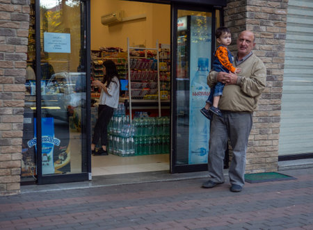 Batumi, Georgia. 23/11/2022 A man holds a child in his arms at the entrance to the store. small trade. Waiting at the store. Sale of products.のeditorial素材