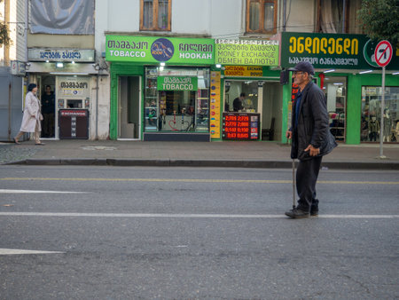 Batumi, Georgia. 11.23.2022 Street scene. A man with a stick walks along the roadway. The beggar asks for alms. urban environment. Beautiful sunny day in the city. road trafficのeditorial素材