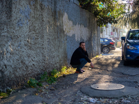 Batumi, Georgia. 23/11/2022 man is squatting against a concrete wall. Rest on the street. hard day. The man is resting.のeditorial素材