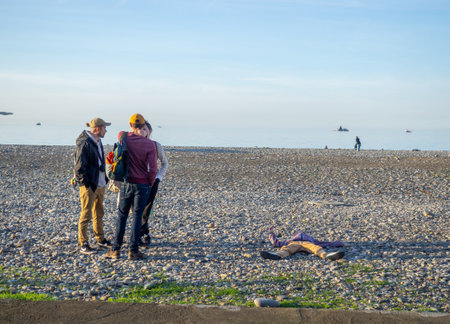 Batumi, Georgia. 18/12/2022 A man in clothes lies on a pebble beach. One lies, and all stand. Indifference.のeditorial素材