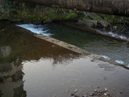 Heating main over the stream. Industry and nature. Fast river in the city. Concrete rapids on the riverの写真素材