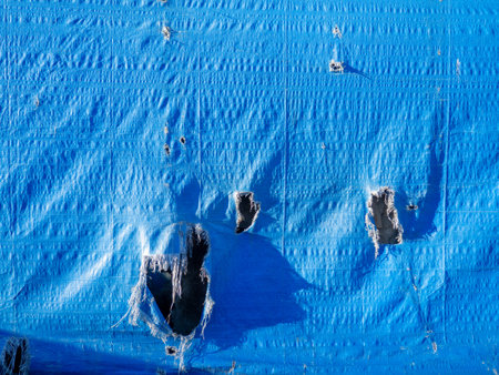 Blue canvas with holes. Leaky fabric. Forgotten. Abandoned. Ragged coatingの写真素材