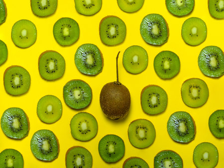 Background of many kiwi slices. One whole in the peel. Sliced kiwi on a yellow background. Raw food concept. sliced fruits. pattern of green ripe fruitsの写真素材