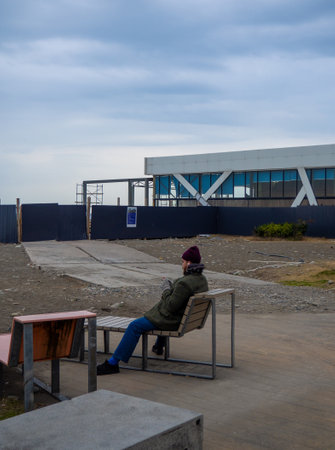 Batumi , Georgia. 01.28.2023  A man sits alone on a sunbed. Beach in winter. Cold weather in the south. The guy sits on a bench and looks at the phone. Photos from ordinary lifeのeditorial素材