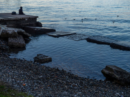 A lonely girl sits on a pier in the port. Sitting on the edge of the water.   concept of loneliness.の写真素材