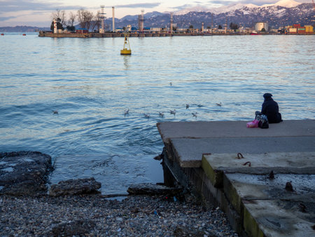 A lonely girl sits on a pier in the port. Sitting on the edge of the water.    concept of loneliness.の写真素材