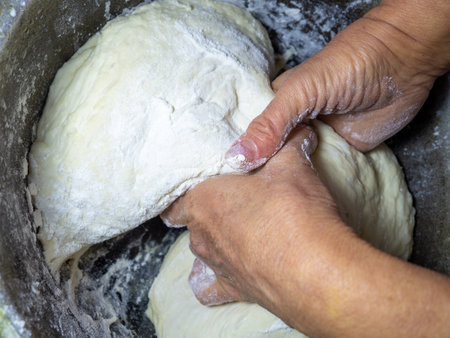 Raw thick dough in the hands of a woman baker. Ready dough for baking in a pan. Test batch. Cook's hands. Opara. Bread preparation. Kneaded yeast dough. Unprepared. calorie product. Bakeryの写真素材