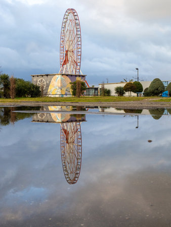 Batumi, Georgia. 02.11.2023 Reflection of a ferris wheel in a puddle. Resort town after the rain. Batumi ferris wheel. Amusement park.のeditorial素材