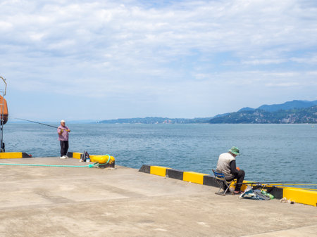 Batumi, Georgia. 07.15.2023 Fishermen are fishing with rods in the port area. People go fishing next to a moored ship. Hobbies for men. Life in a port cityのeditorial素材