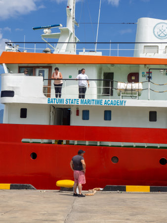 Batumi, Georgia. 07.15.2023 Scientific ship moored to the shore. Training boat mooring. The port worker is preparing to tie the mooring line. Ship Cadet.のeditorial素材
