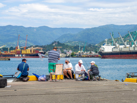 Batumi, Georgia. 07.15.2023 Fishermen in the port of Batumi. Fisherman on the Black Sea. Hobby. Industrial zone. Fishing from the pier. rodsのeditorial素材