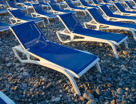 Beach chairs. Lots of empty sunbeds on the pebbles. The concept of commerce on the beach. Sunbed rental at the resort. At sunset. Rest of people on the sea.の写真素材