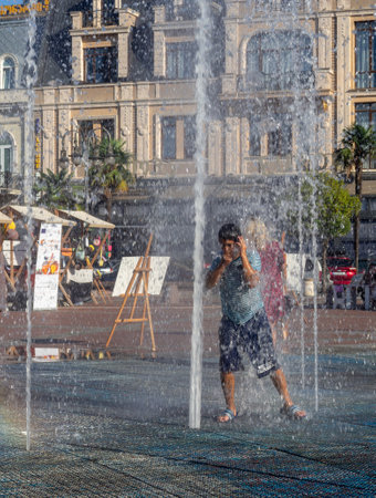 Batumi, Georgia. 08.19.2023  Boy is playing in the fountain. Wet child in the fountain.  Wet clothes on the boy. Children's pranks in the city. Salvation from the heat. Childhood concept. Lots of splashing waterのeditorial素材