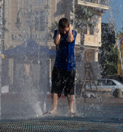 Batumi, Georgia. 08.19.2023  Boy is playing in the fountain. Wet child in the fountain.  Wet clothes on the boy. Children's pranks in the city. Salvation from the heat. Childhood concept. Lots of splashing waterのeditorial素材
