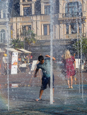 Batumi, Georgia. 08.19.2023  Boy is playing in the fountain. Wet child in the fountain.  Wet clothes on the boy. Children's pranks in the city. Salvation from the heat. Childhood concept. Lots of splashing waterのeditorial素材