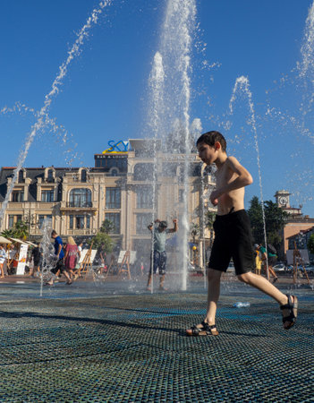 Batumi, Georgia. 08.19.2023   Boy is playing in the fountain. Wet child in the fountain.  Wet clothes on the boy. Children's pranks in the city. Salvation from the heat. Childhood concept. Lots of splashing waterのeditorial素材